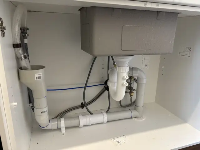 New plumbing under a kitchen sink: sink waste and trap, dishwasher drain hose and water connections