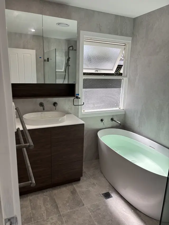Finished bathroom with a freestanding bath, wall-mounted bath spout and basin mixer, and a timber vanity
