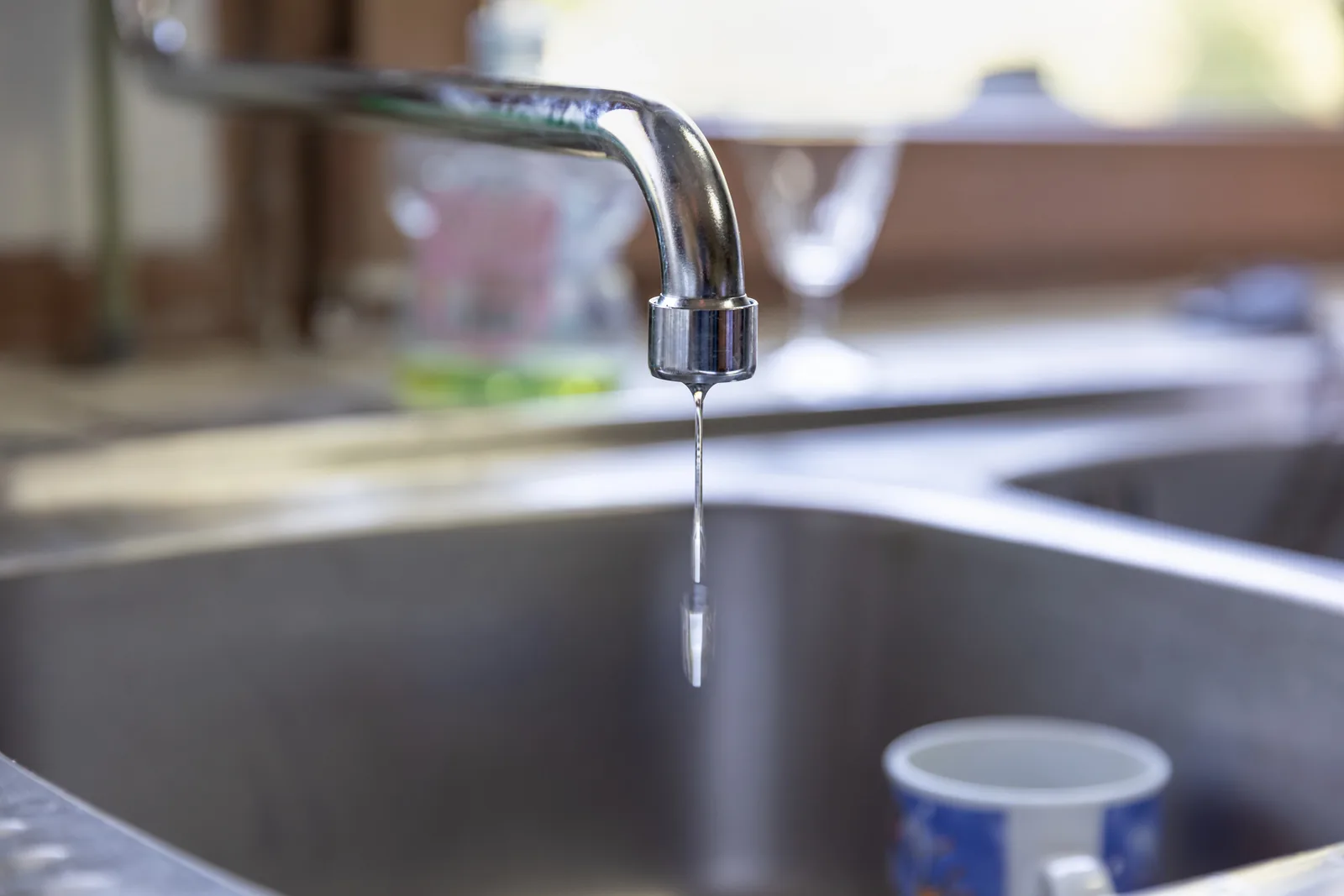 Water dripping from a leaking chrome kitchen tap into a stainless steel sink