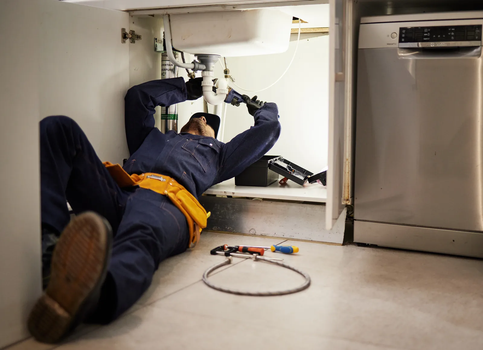 Plumber lying under a kitchen sink repairing pipework during an emergency callout